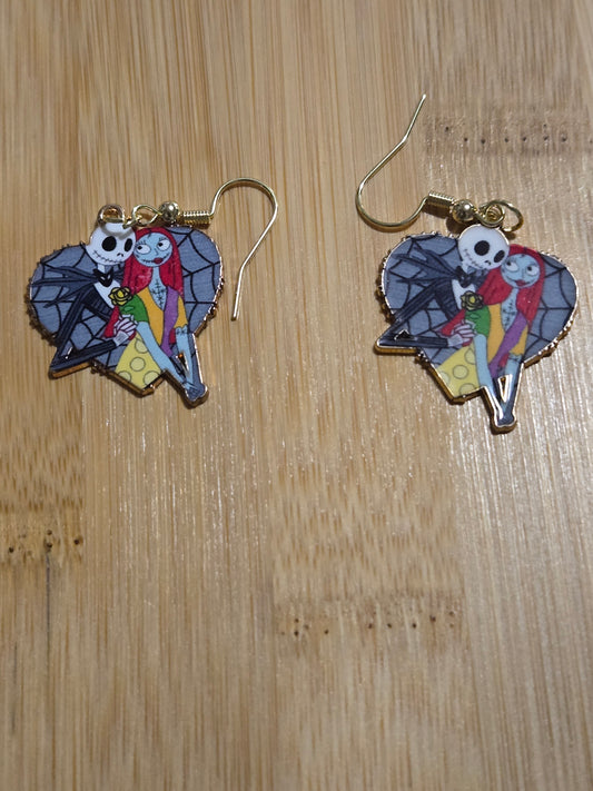 A pair of earrings featuring a gray heart shape with jack and sally, displayed on a wooden surface.