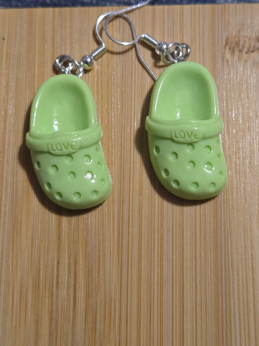 A pair of green croc-shaped earrings on a wooden surface.