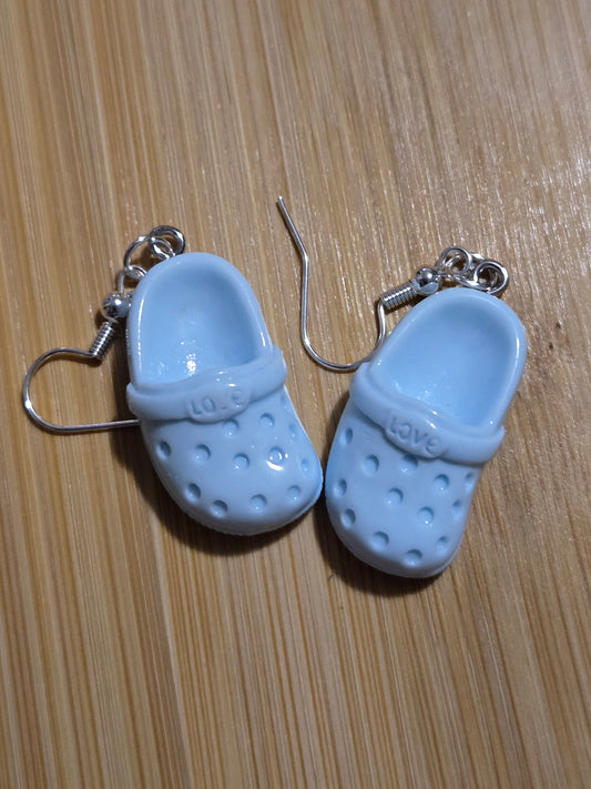 A pair of light blue croc-shaped earrings on a wooden surface.
