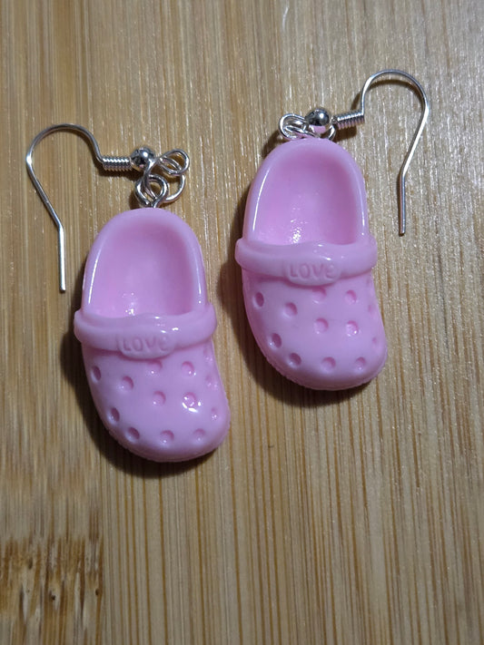 A pair of light pink croc-shaped earrings on a wooden surface.