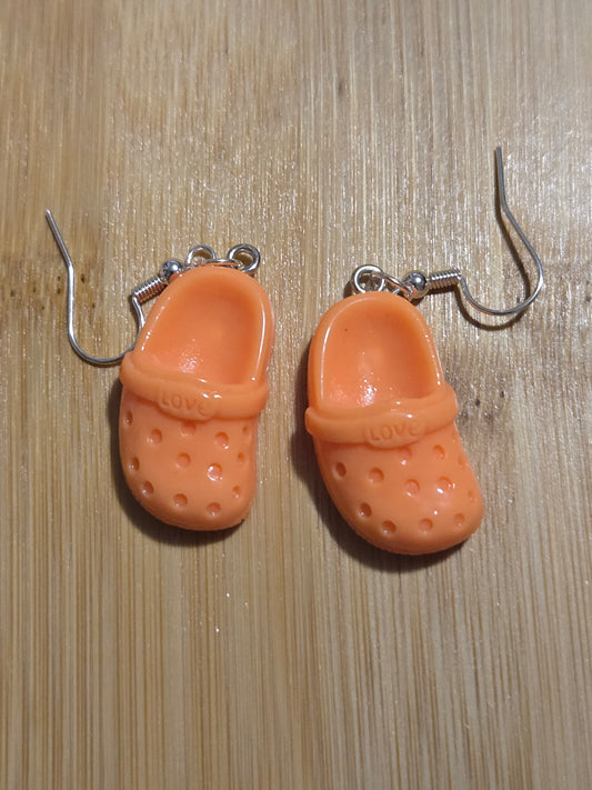 A pair of orange croc-shaped earrings on a wooden surface.