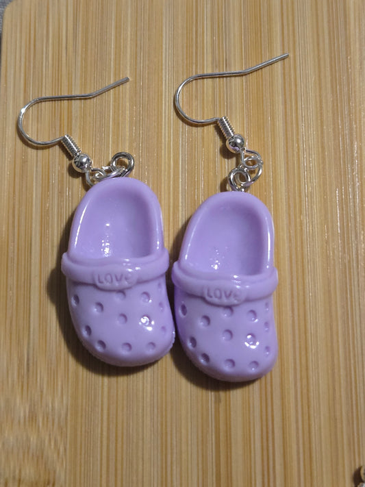 A pair of purple croc-shaped earrings on a wooden surface.