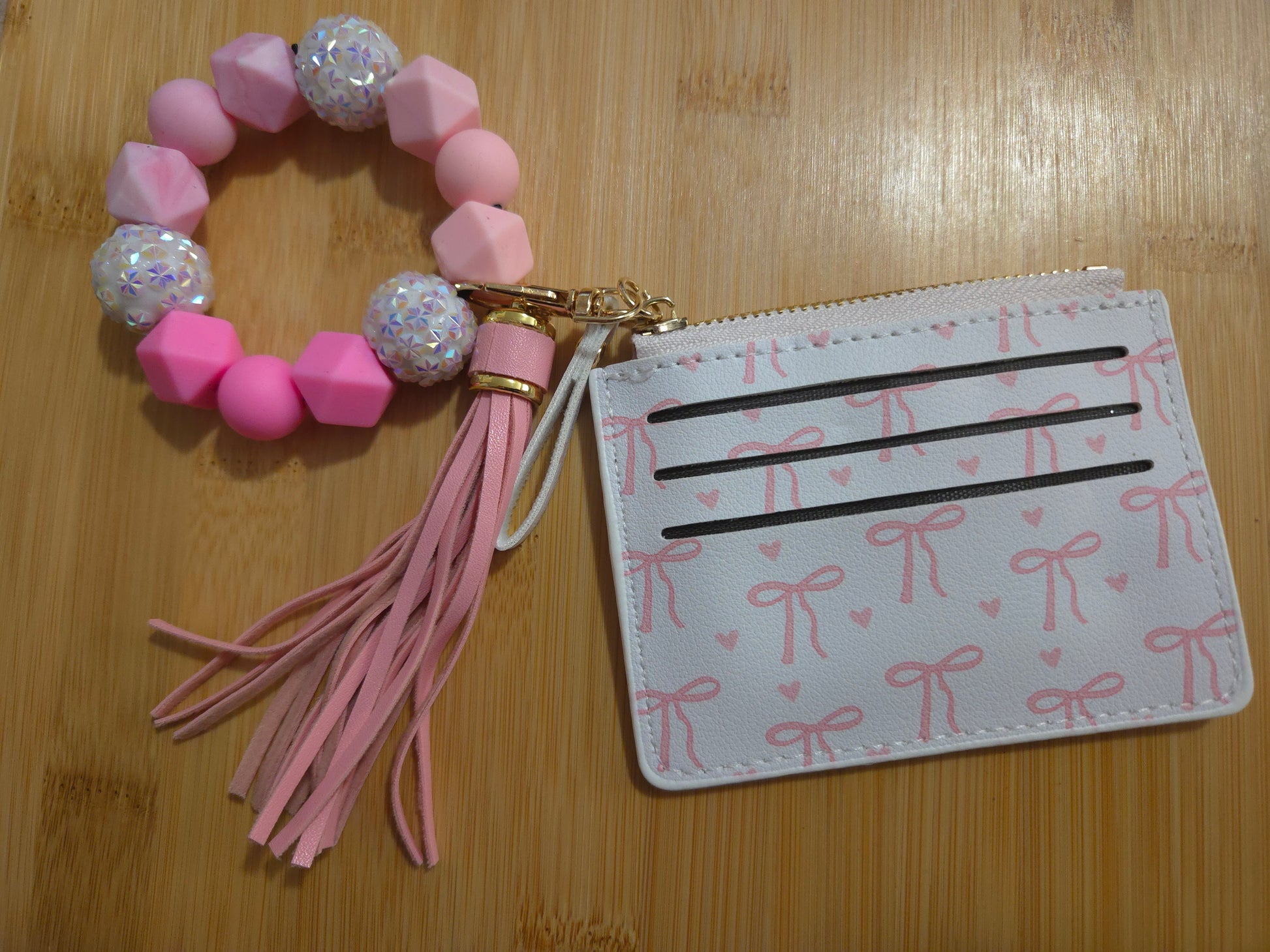 Pink cardholder with tassel and decorative keychain on a wooden surface