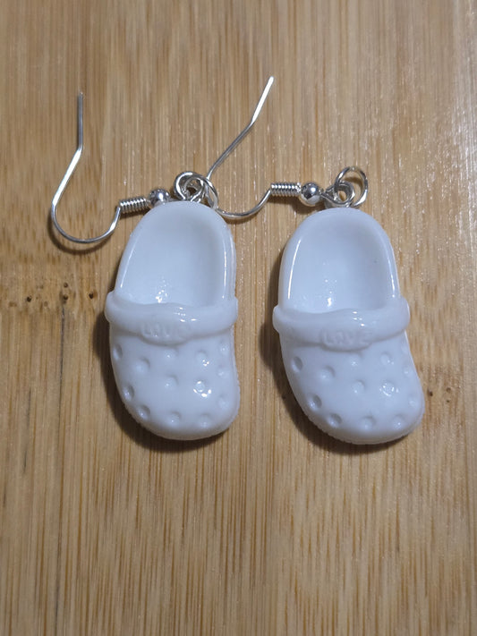 A pair of white croc-shaped earrings on a wooden surface.