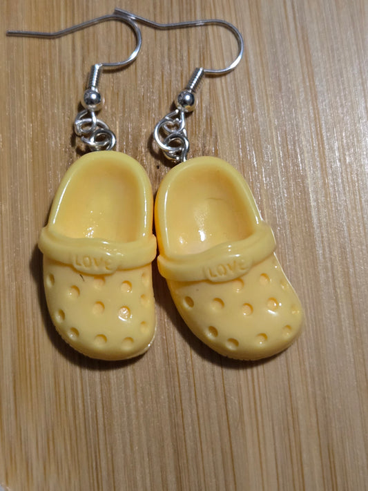 A pair of yellow croc-shaped earrings on a wooden surface.